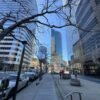 Urban cityscape with tall buildings, busy sidewalk, and clear blue sky.